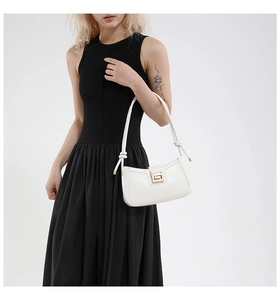 Close-up of minimalist cream leather underarm bag with gold buckle and knot handle detail