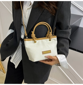 Detail of hand-woven bucket bag featuring a contrast brown leather tag and long strap