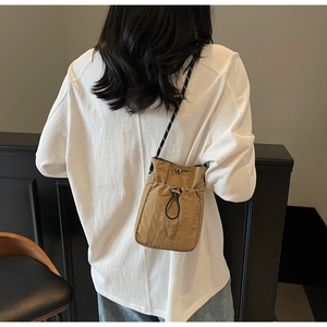 Detail of khaki drawstring crossbody bag with woven strap shown on a model