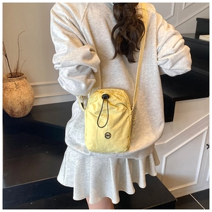 Detail of a yellow water-resistant nylon drawstring crossbody bag on a female model