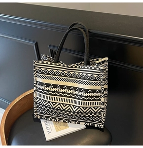 Detail view of canvas tote bag with black and white geometric patterns on a leather chair