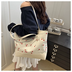 Detailed side view of off-white canvas tote bag featuring red cherry embroidery on a model