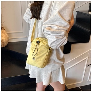 Detail of light yellow nylon crossbody bag with drawstring closure and metal logo