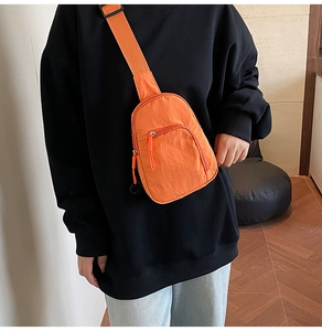 Gros plan du sac bandoulière orange vif avec sangle noire réglable et fermetures éclair
