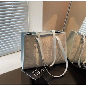 Detail of light blue tote bag featuring white floral relief and elegant tassel pendant