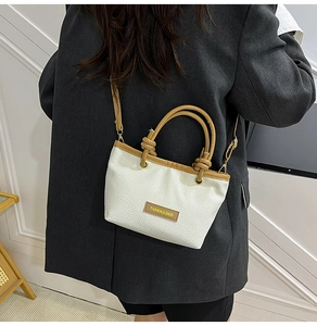 Model shot of a white woven bucket bag with brown leather trim and adjustable strap