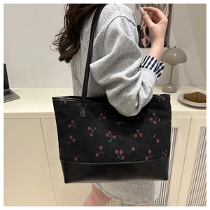 Lifestyle shot of black canvas tote bag with red cherry print and leather straps
