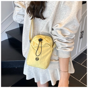 Close-up of pale yellow nylon crossbody bag with drawstring closure and outdoor style logo