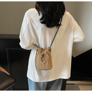 Detail of khaki drawstring crossbody bag featuring woven rope strap on white clothing