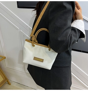 Detail view of woven bucket bag with brown leather trim and fashion brand tag on a model
