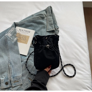 Detail of black drawstring crossbody phone bag with woven shoulder strap on a bed