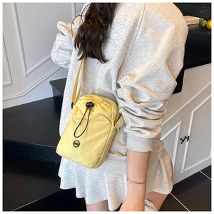 Detail view of light yellow waterproof nylon crossbody bag worn by a model in casual setting