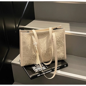 Close-up of embossed floral tote bag with elegant tassel charm and textured leaf patterns