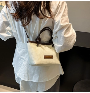 Detail of hand-woven bucket bag featuring a brown leather label and knot handle design