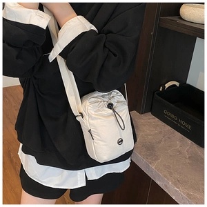 Detail of adjustable strap and drawstring closure on cream nylon crossbody bag