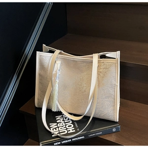 Detail of cream large tote bag with floral jacquard texture and tassel on wooden stairs