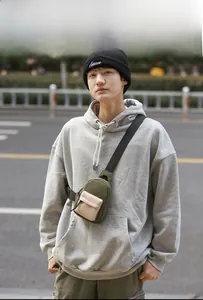 Detail of army green and beige crossbody bag shown on model in urban street setting