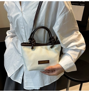 Detailed view of woven straw bucket bag with dark brown leather handles and brand tag