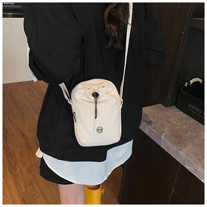 Detail view of the cream-colored nylon drawstring crossbody bag worn on shoulder
