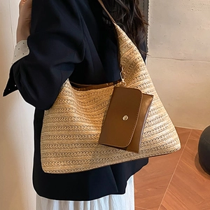 Straw woven tote bag with brown leather pouch shown on shoulder in a minimalist room