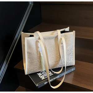 Close-up of cream tote bag with floral texture and tassel on wooden stairs