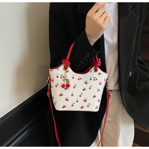 Détail du sac seau blanc avec motif cerises et poignée rouge tressée sur un mannequin