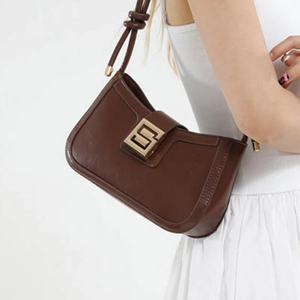 Minimalist brown leather shoulder bag with a gold buckle shown on a model