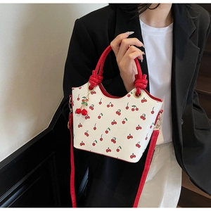 Détail du sac cabas blanc à motif cerise avec anse en corde rouge et pendentif