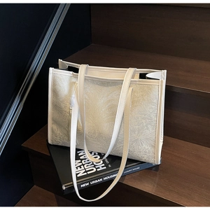 Close-up of embossed floral pattern on off-white tote bag resting on art books