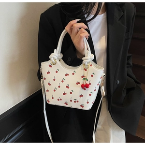 Détail du sac cabas blanc à imprimé cerises avec poignée nouée porté par un mannequin