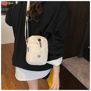 Detail of cream nylon crossbody bag featuring a drawstring closure and circular brand logo