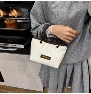 Detail view of woven square bag with cream texture, brown knotted handles and logo