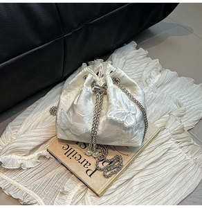 Close-up of white satin bucket bag with floral texture, butterfly embroidery and pearl strap