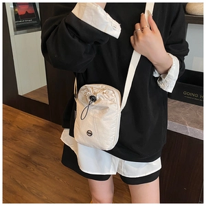 Detail of cream nylon crossbody bag with drawstring closure and metal logo emblem