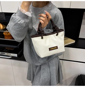 Detail of hand-woven bucket bag with cream fabric texture and brown leather trim handle
