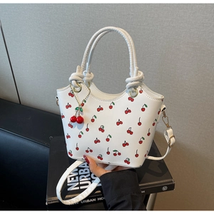 Détail d'un sac seau blanc à imprimé cerise avec ferrures dorées et breloque en métal