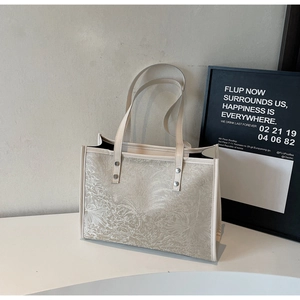 Close-up of beige tote bag with floral jacquard texture and durable rivet handles