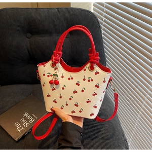 Détail d'un sac seau en cuir blanc avec imprimé cerise et charms décoratifs