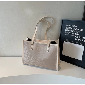 Close-up of cream tote bag featuring grey floral patterns and side silver rivet details