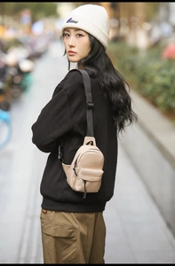 Detail view of a beige crossbody chest bag with adjustable black strap worn by a model