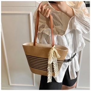Close-up of a woven straw tote with black stripes and a delicate white lace bow detail