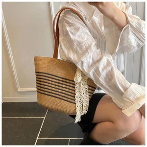 Detail of striped woven straw tote bag with brown leather handles and lace ribbon accent