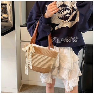 Detail of striped straw tote bag featuring leather handles and lace bow decoration