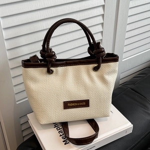 Straw woven tote bag with brown leather handles and brand plaque on a book