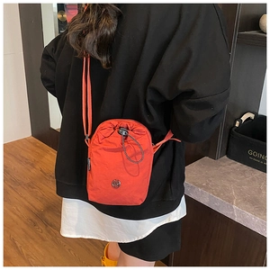 Detail of orange drawstring nylon crossbody bag worn over a black hoodie for contrast