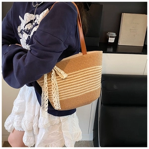 Detailed close-up of woven straw tote bag featuring white lace ribbon and brown leather handle