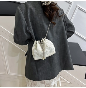 Detailed view of white lace butterfly embroidery and pearl drawstring on a bucket bag
