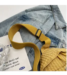 Detail of adjustable woven strap on yellow checkered canvas crossbody bag over denim