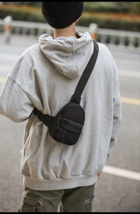 Back view of a black nylon waterproof crossbody bag worn by a model in casual attire