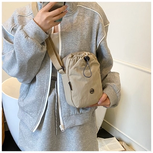 Detail of compact beige nylon drawstring crossbody bag styled with casual grey sportswear